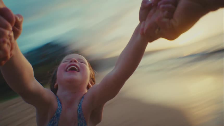 POV of parent spinning laughing young daughter by her hands on tropical beach at sunset