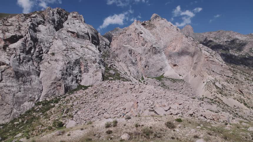 A rocky mountainous landscape with a large pile of loose rocks and a small figure a hiker walking along a path at the base of the mountain