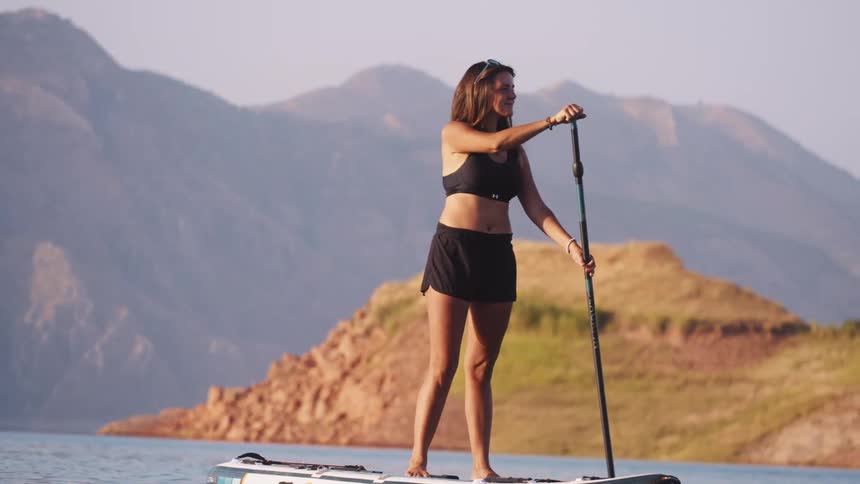 Smiling woman paddleboarding peacefully on inflatable board on the lake