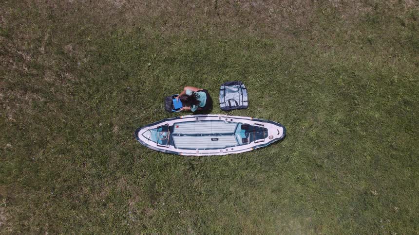 Girl seen from above sitting in a meadow with a canoe beside her