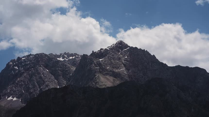 A mountain peak rises against a backdrop of a blue sky dotted with fluffy white clouds