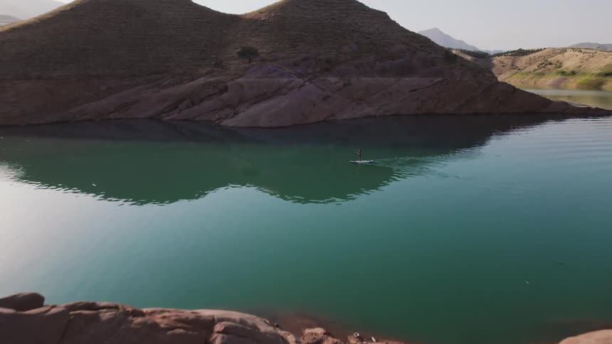 A paddle boarder in the middle of a lake surrounded by mountains