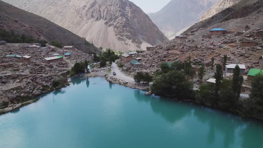 A vibrant turquoise lake sits nestled within a valley surrounded by towering arid mountains and scattered settlements