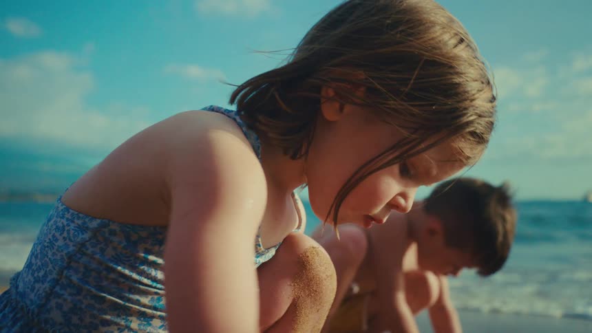 kids in swimsuits play in a sandy beach digging a hole near the ocean on a sunny day