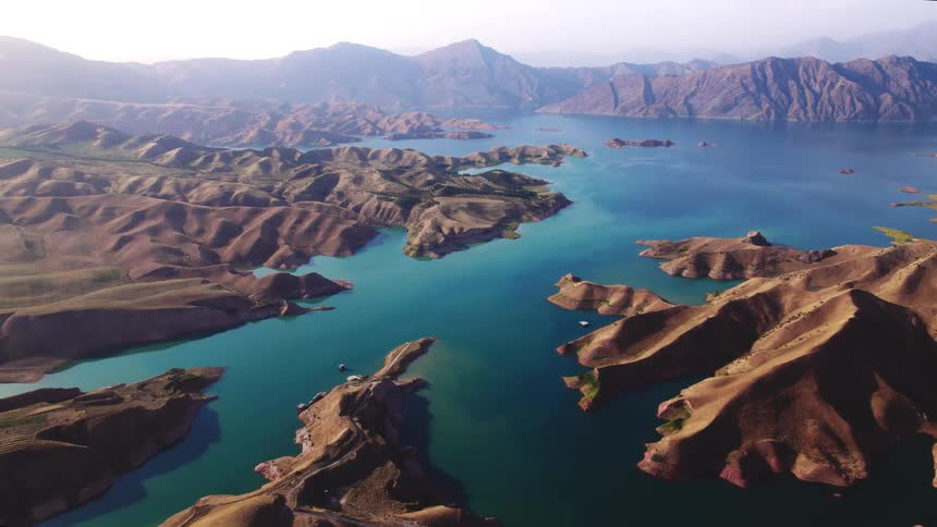 Aerial view of a vast landscape of rugged brown mountains surrounding a deep blue lake