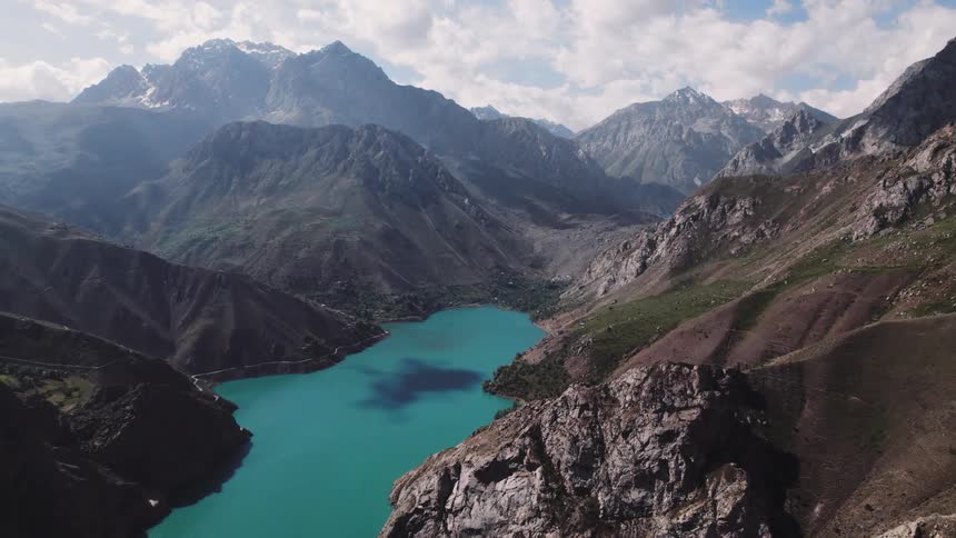 An aerial view of a turquoise lake nestled amidst rugged mountain peaks and valleys