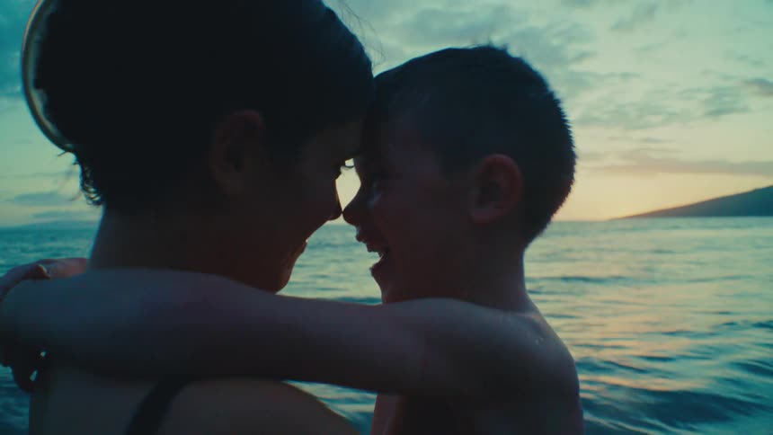Mother embracing five-year-old son on tropical beach at sunset