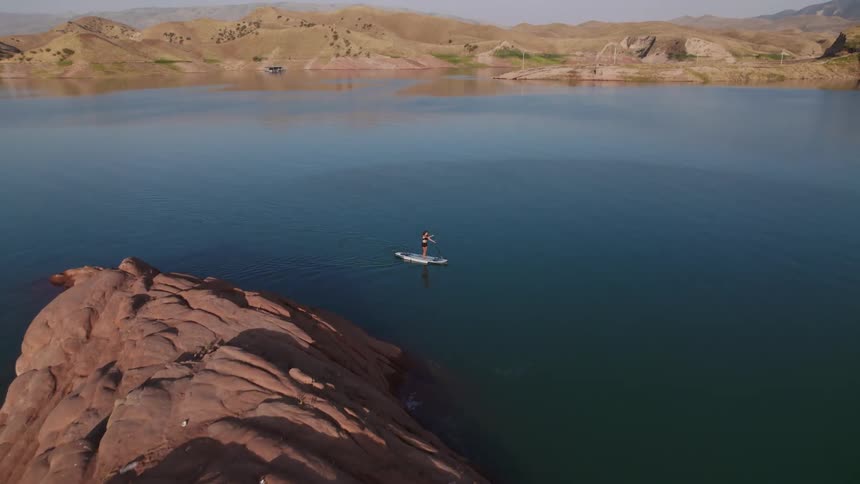 A person is using an oar to move a paddle board across a lake in the mountains