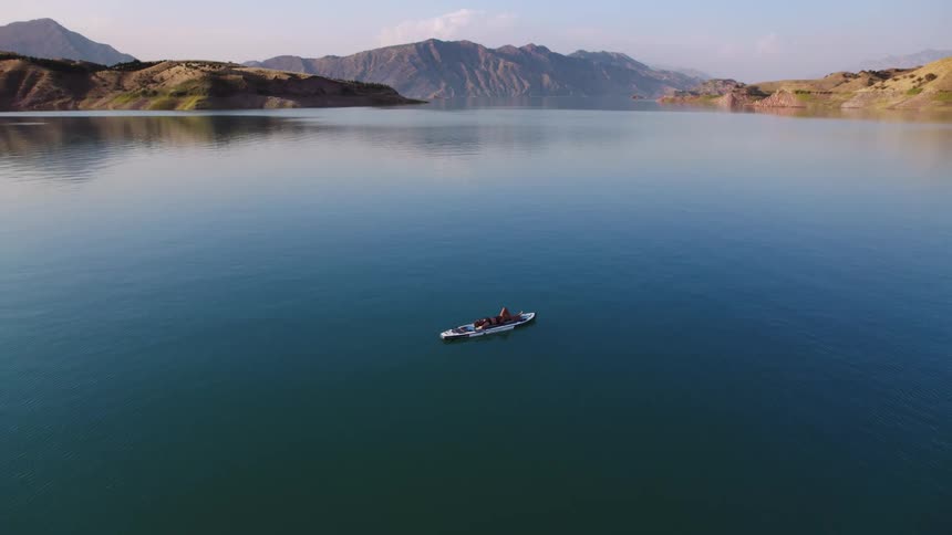 A person enjoys resting on a board floating on a serene lake surrounded by mountains in the gentle light of morning