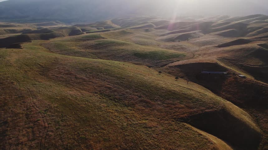 Aerial view of a vast undulating landscape with rolling hills and valleys bathed in sunlight