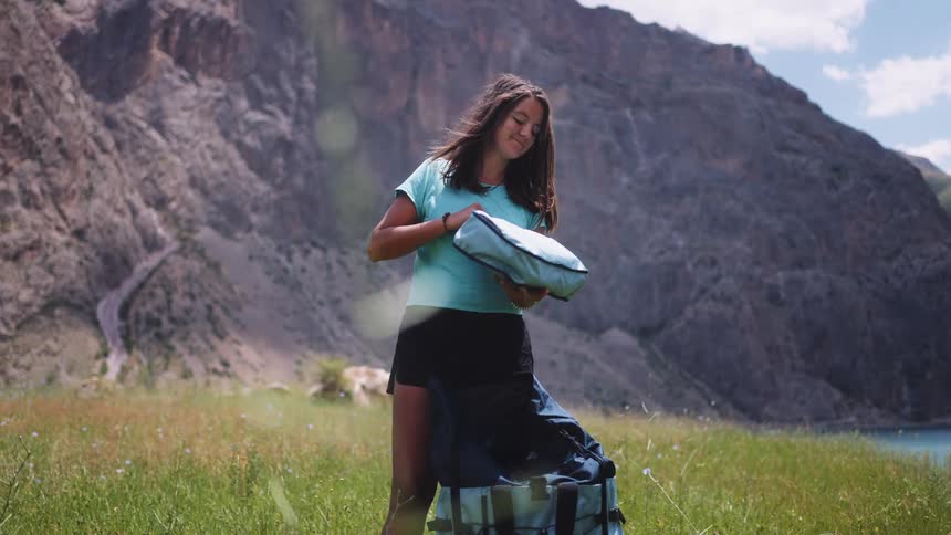 A young woman stands in front of a mountain and pulls a small bag out of a larger one