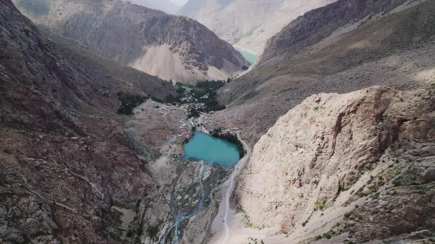 An aerial perspective flies towards a rugged coastline where arid rolling hills meet the distinctively colored water below