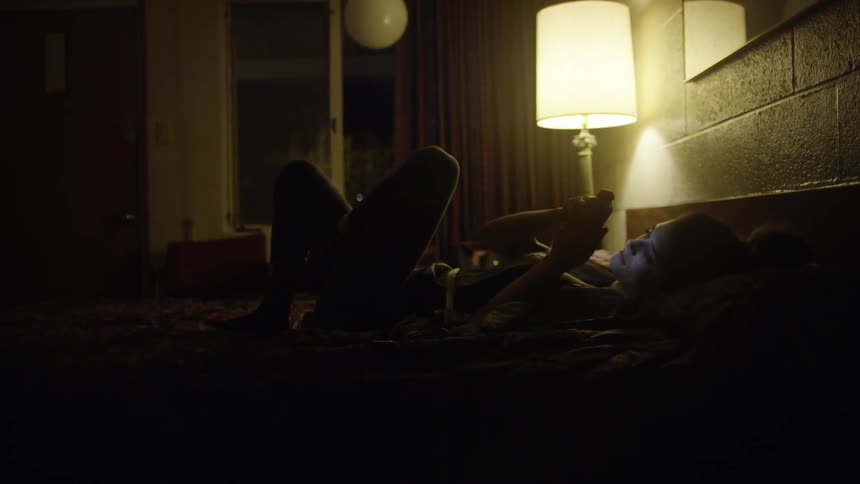 A woman lays in bed while using her phone