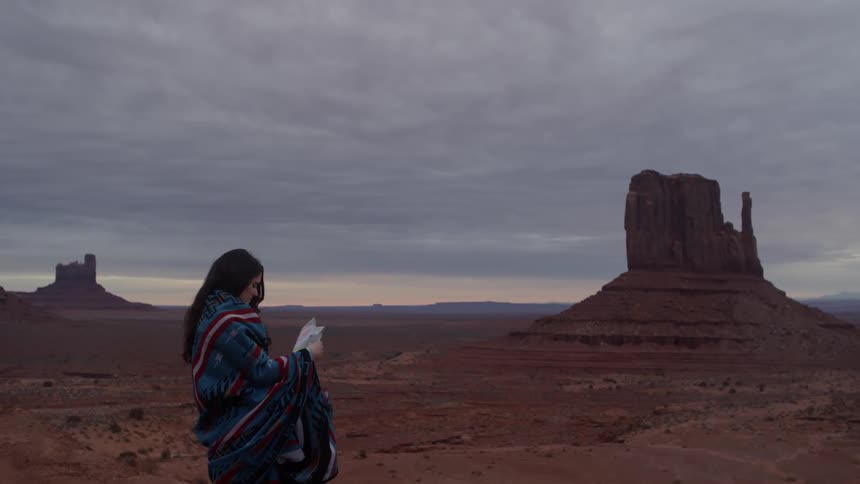 A woman wrapped in a blanket standing out in the desert