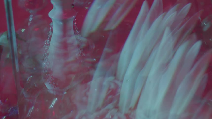 A static pinktinted scene shows an arrangement of stemware crystals and a necklace with layered light patterns projected across the surfaces casting reflections and abstract visual textures