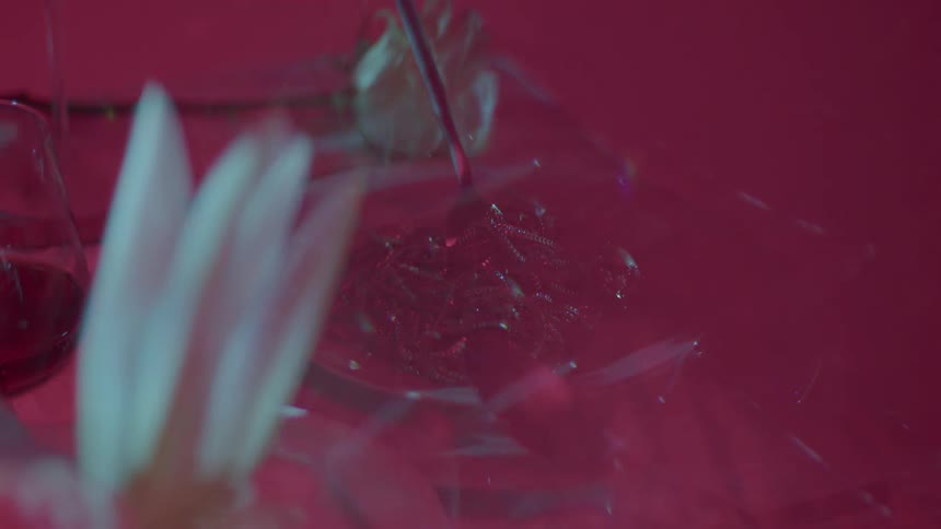 Light reflects off glass figures on a pink table adorned with petal flowers in the foreground