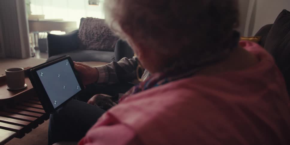 An elderly man and woman talk as they sit on a couch and look at a tablet