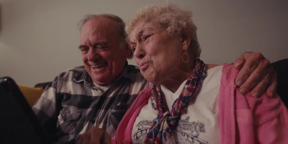 A woman waves at the tablet while talking and smiling