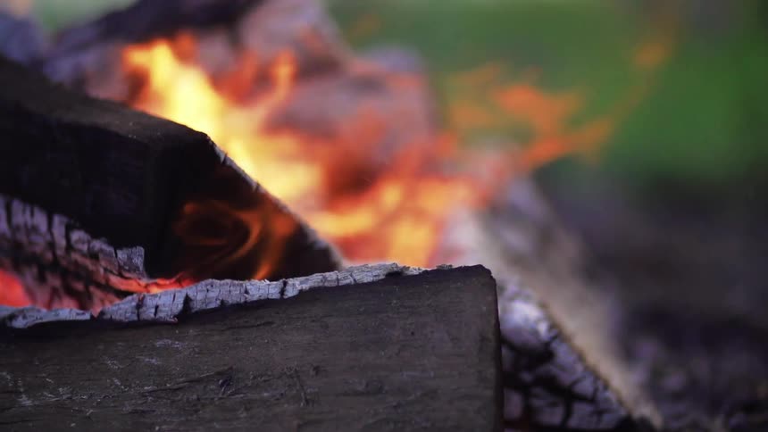 A campfire burns during the day on flat grassland