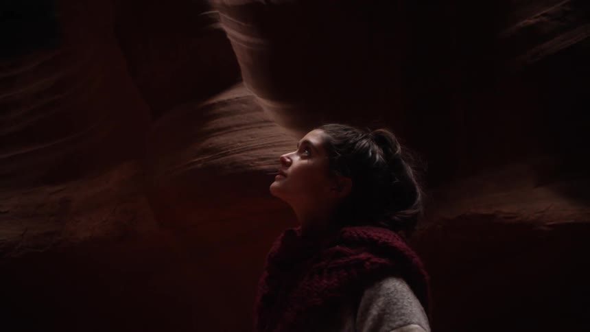 A woman is walking in a dark cavern looking up