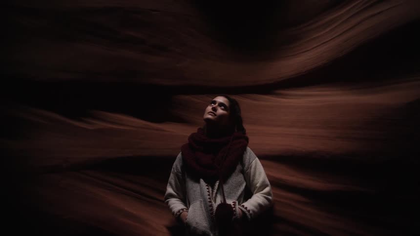 A woman leans against the cavern wall with her eyes closed