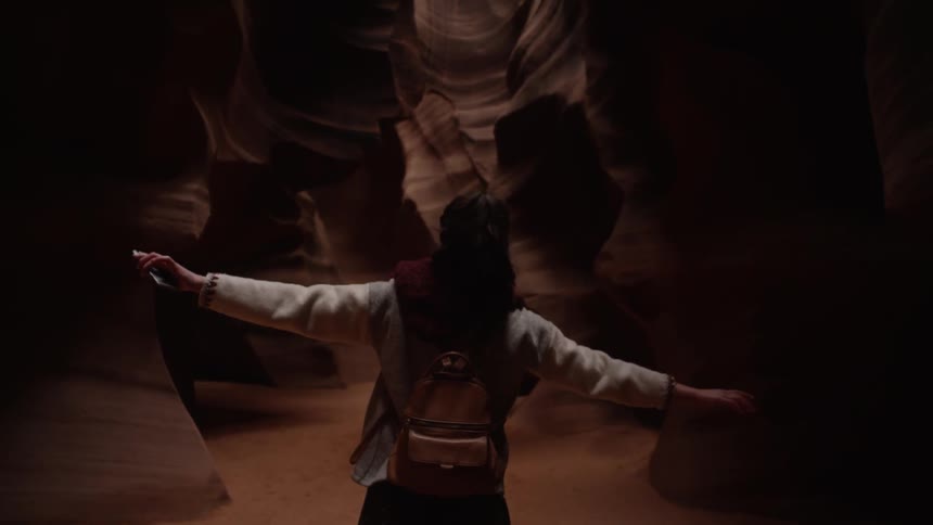 A person walks slowly in a dark cavern arms stretched out