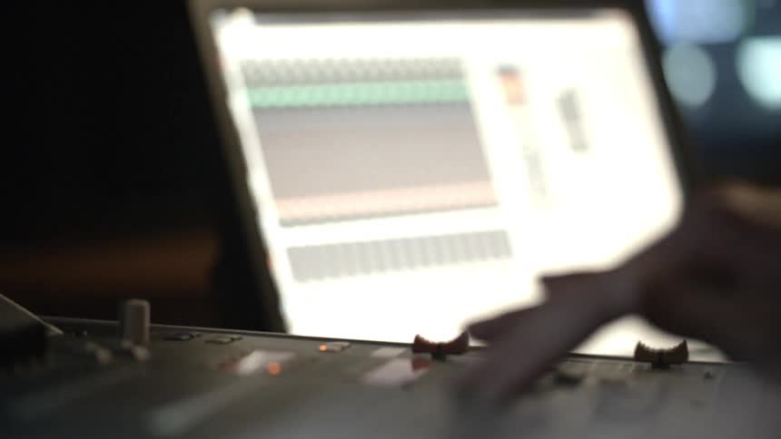 A person adjusts faders on a mixing board