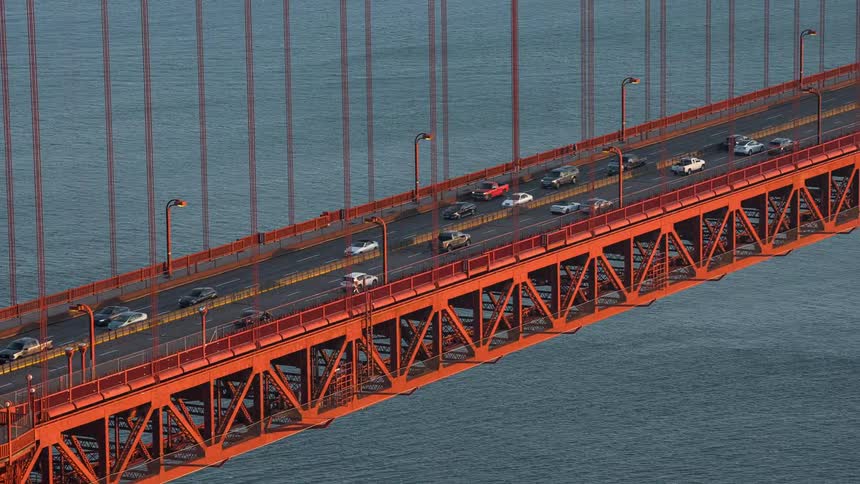 Vehicles travel along the multilane roadway of the iconic orange golden gate bridge supported by its massive towers and intricate truss system over the water