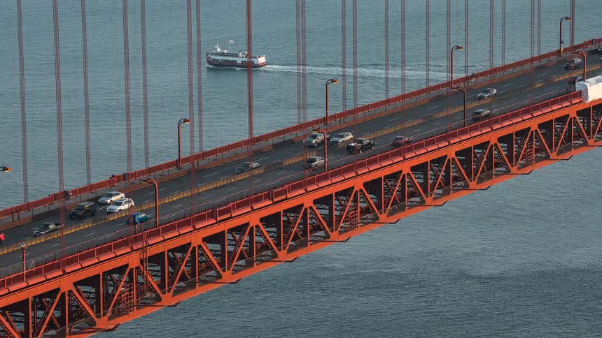 Cars traveling at high speed across a bridge while a boat goes by in the background