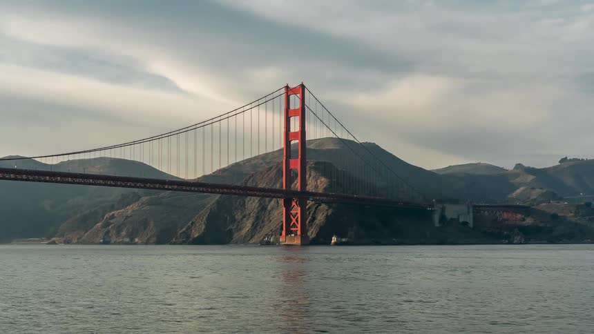 The iconic golden gate bridge with its distinctive reddishorange hue stretches horizontally across the frame its towers and suspension cables clearly visible against the muted tones of the sky and surrounding landscape