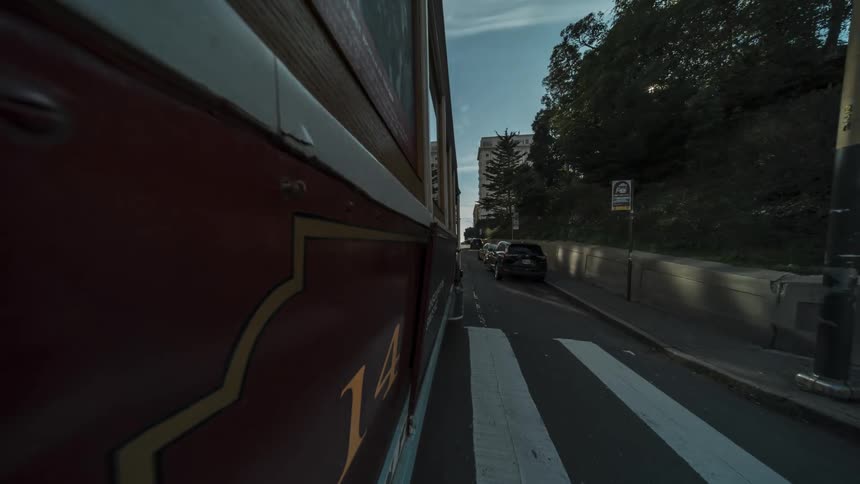 A fast motion blurred exterior shot capturing the side of a red vintage tram traveling down a city street