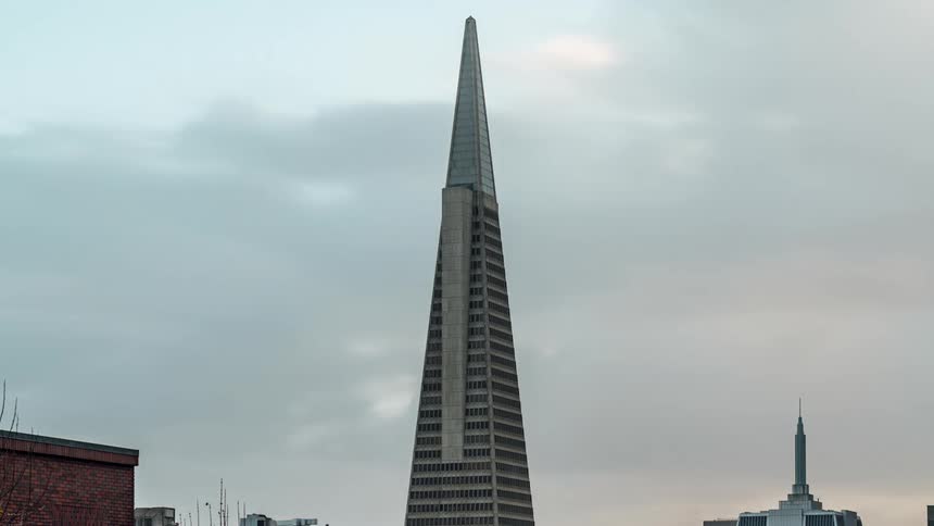 A timelapse shows clouds speeding past the distinct spire of the transamerica pyramid skyscraper against an overcast sky