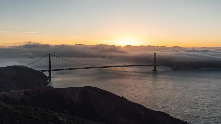 The clouds flow over the tall bridge at sunrise