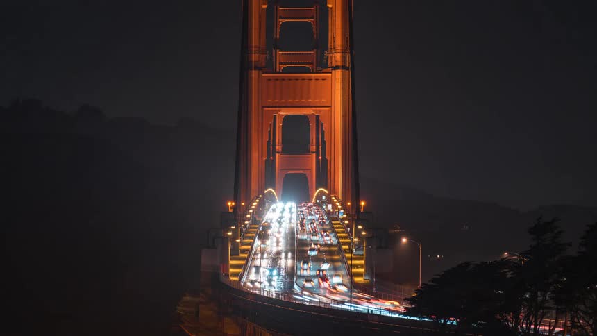 A static shot of the golden gate bridge at night shows vehicles driving in both directions as timelapse motion creates continuous light trails across the illuminated span