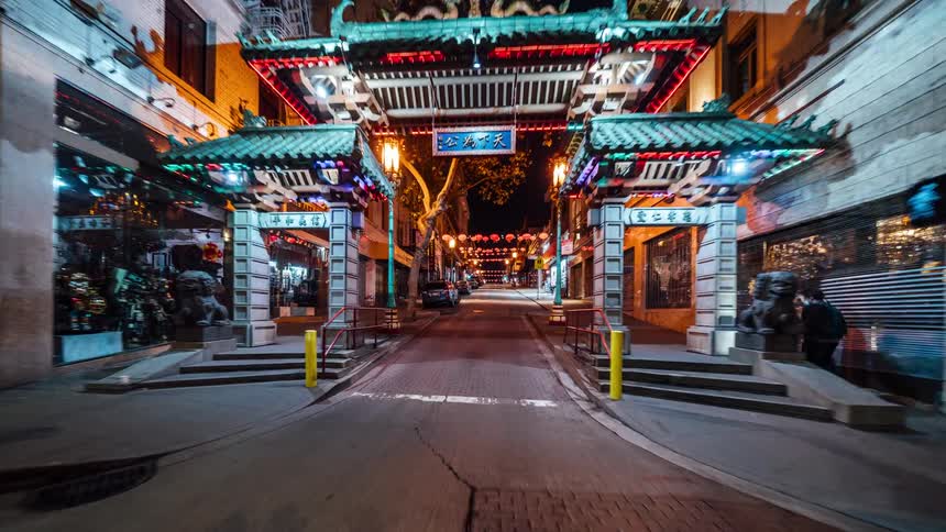 A brightly lit ornate gate with a pagodastyle roof spans a narrow street at night