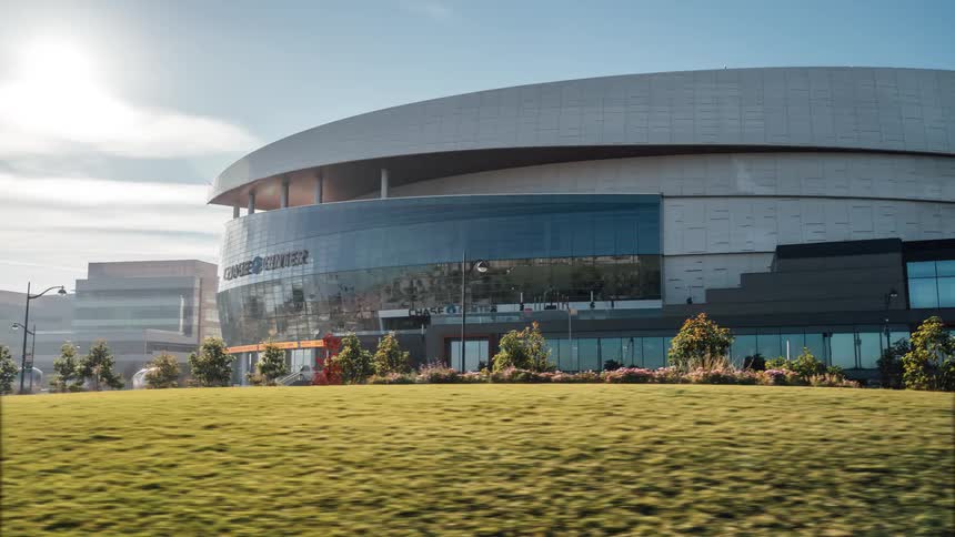 A view of the chase center arena from across a green space with street side parking