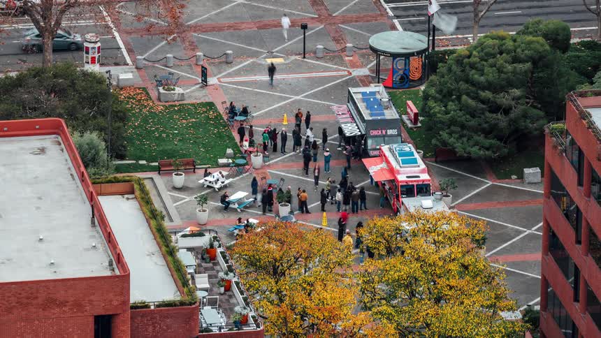 In the courtyard there are three food trucks lined up and a large group of people lined up at each one