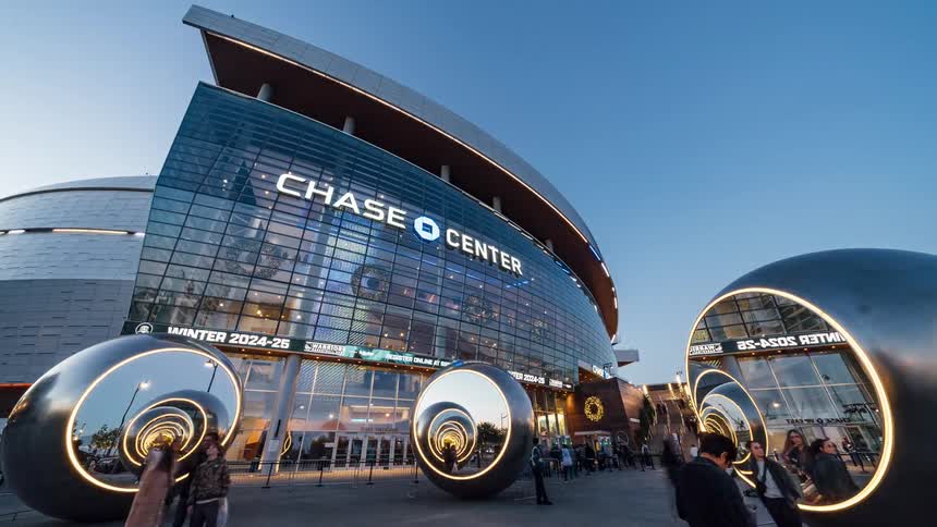 People coming and going outside an arena with advertisements scrolling on a digital banner