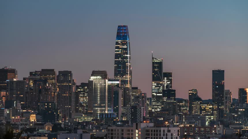 The san francisco skyline at dusk shows city lights twinkling against the darkening sky highlighting the salesforce tower as a prominent feature