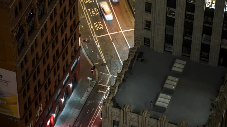 An aerial nighttime view of a city street intersection with painted lane markings for taxi and bus framed by the illuminated facades of tall buildings