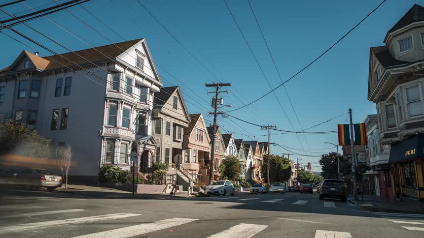 A street level view depicts a row of victorianstyle houses lining a street corner under a clear sky
