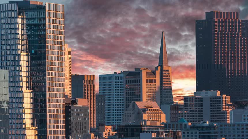 A cityscape featuring the transamerica pyramid with tall buildings framing the central view under a dramatic cloudy sky