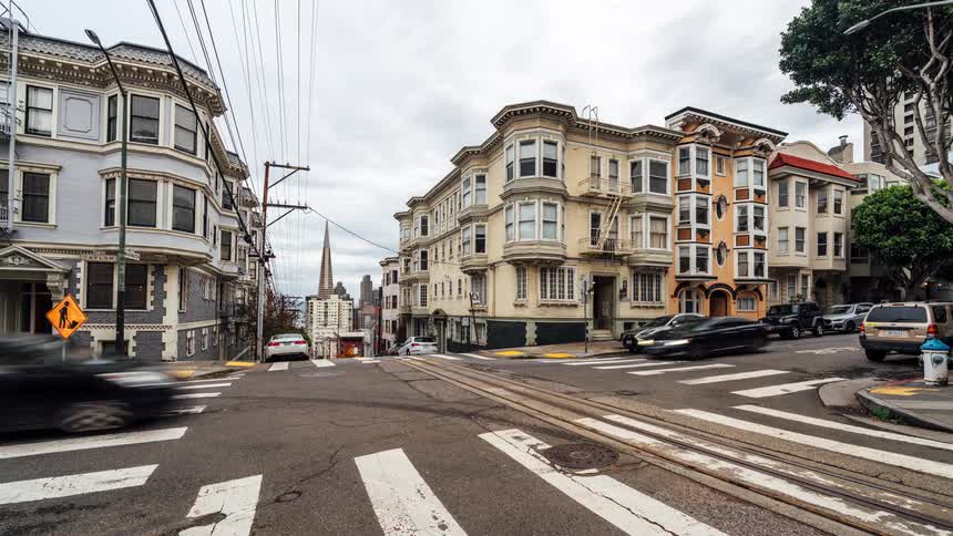 Trolley and cars take turns passing through an intersection in an urban neighborhood