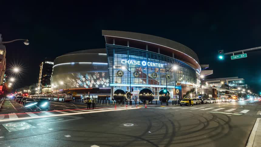 Pedestrians and traffic move past an arena in a city at night