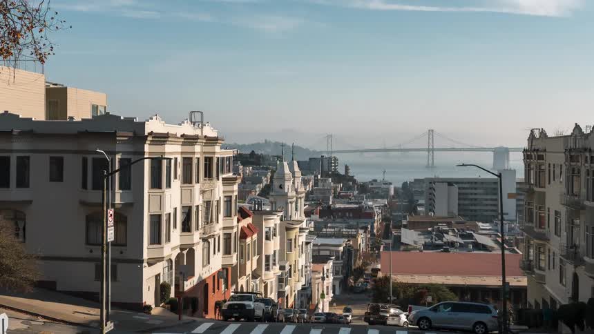 Traffic crosses through a busy intersection on a city street leading down a hill towards the waterfront on a foggy day