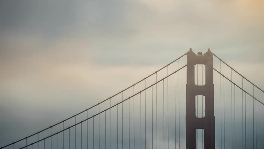 The golden gate bridge in san francisco emerges from thick fog in a softly lit scene