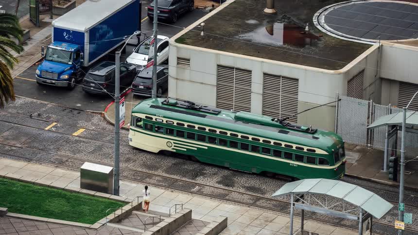 A vintage green and cream streetcar navigates the tracks through a city intersection