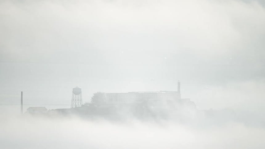 Enveloped in thick rolling fog alcatraz islands structures including its water tower are barely visible through the heavy haze covering the bay
