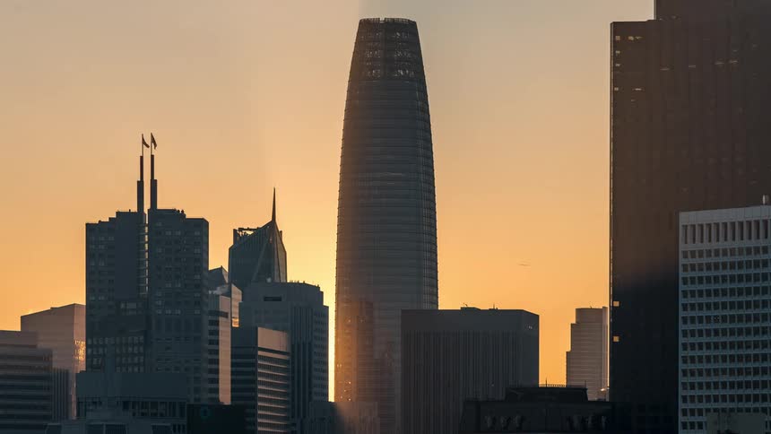 A cityscape features the silhouette of the salesforce tower against a warm sunset colored sky flanked by other buildings