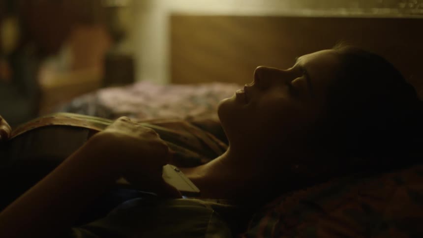 A young woman is holding a cellphone and lying in bed